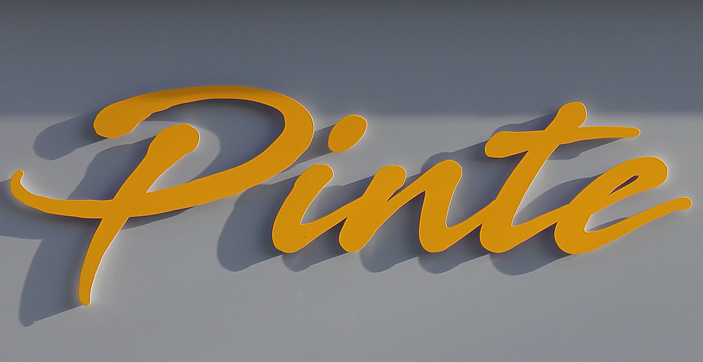 Gelber Schriftzug ‚Pinte‘ in Schreibschrift auf grauem Hintergrund