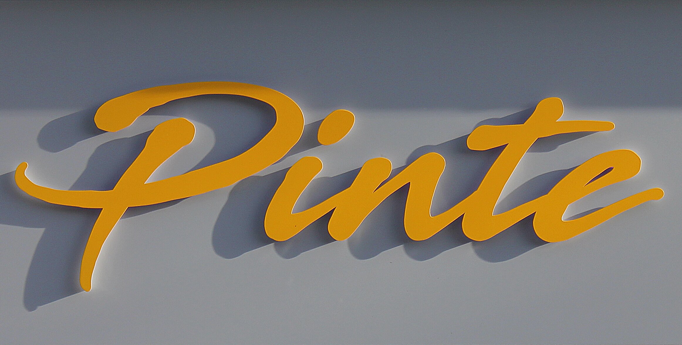 Gelber Schriftzug ‚Pinte‘ in Schreibschrift auf grauem Hintergrund